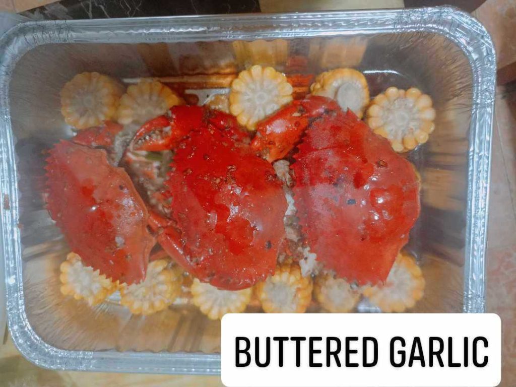 Close-up of butter garlic crab served on a plate, coated in golden garlic butter sauce